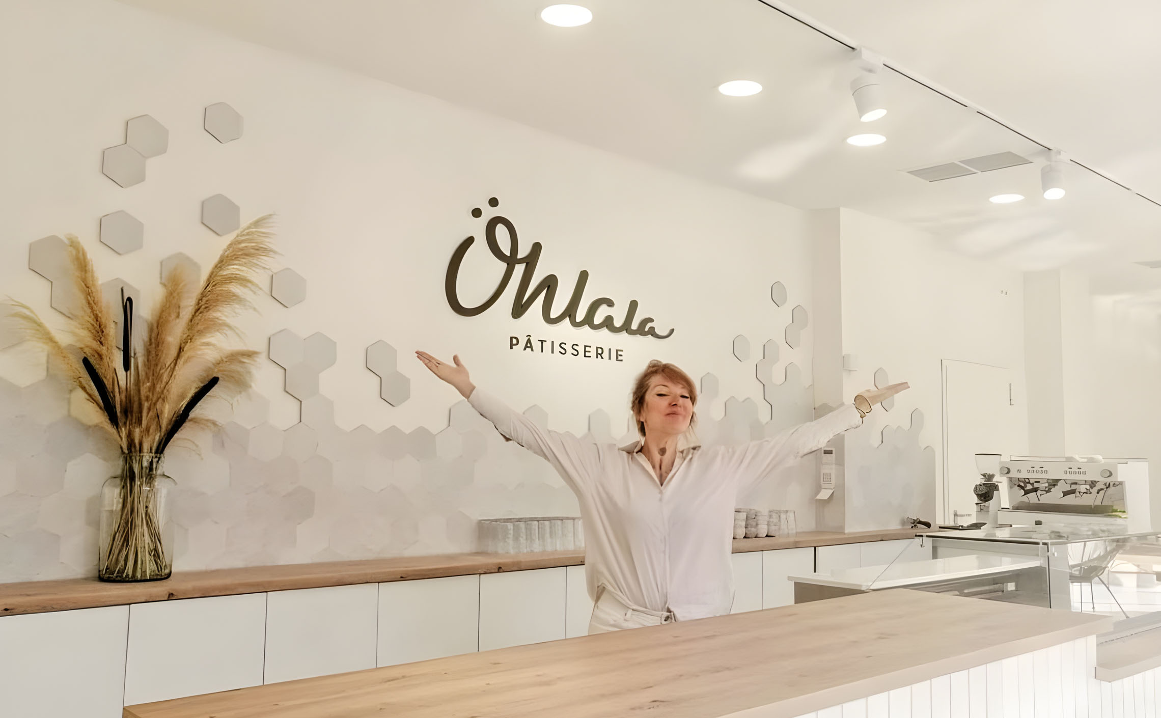 Alina Petrea with arms wide open in front of the counter of the Ohlala Pâtisserie